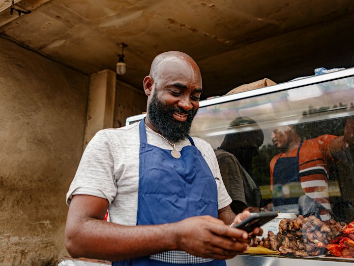 Food stall owner in an apron smiling at his phone