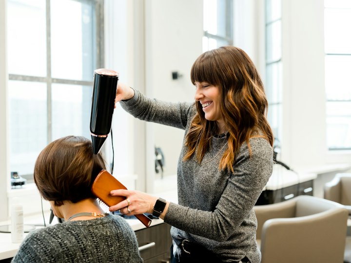 Hairstylist blow-drying a client's hair in a bright salon